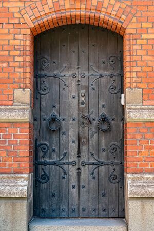 Closeup of an beautiful old black rustic wooden door entrance on a brick building. Ornated decorative iron fittings.の写真素材