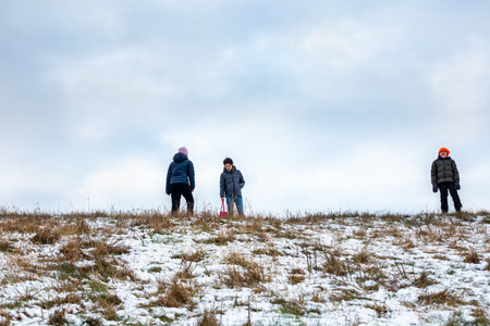 Low angle view of three children outdoor on a grassy snow hill with sky in the background.の写真素材