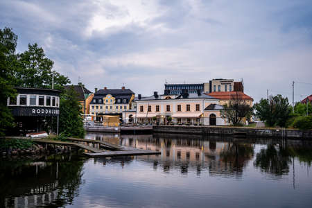 NORRKOPING, SWEDEN - JULY 27, 2021: Beautiful cityscape view of a old black vintage boathouse with buildings by the water with water reflections and incidental people in Norrkoping Sweden July 27, 2021.のeditorial素材
