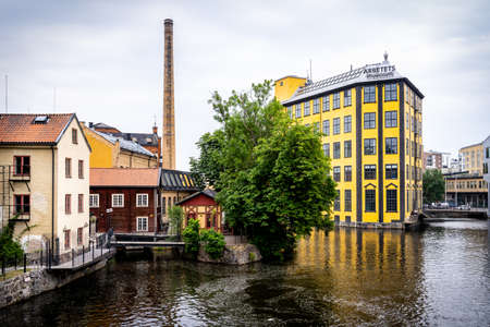 NORRKOPING, SWEDEN - JULY 27, 2021: Beautiful cityscape view of the old yellow industrial building Strykjarnet near water reservoir with reflections. Arbetets Museum with incidental people in Norrkoping Sweden July 27, 2021.のeditorial素材