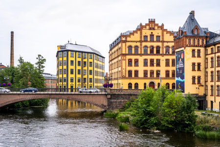 NORRKOPING, SWEDEN - JULY 27, 2021: Beautiful old yellow industrial building with bridge over river...
