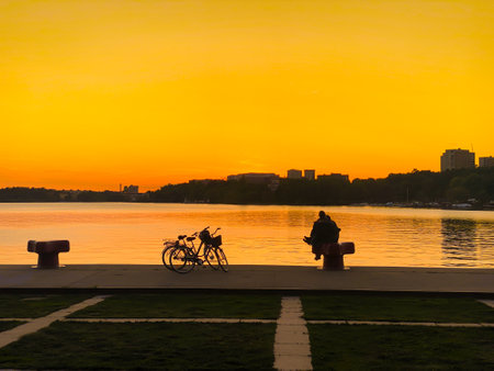STOCKHOLM, SWEDEN - MAY 22, 2022: Beautiful spring city sunset with two people sitting by waters edge with orange sky in Stockholm Sweden May 22, 2022.のeditorial素材