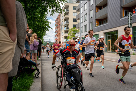 STOCKHOLM, SWEDEN - JUNE 4, 2022: City street front view of runners and disabled person in wheelchair at Stockholm Marathon with incidental people in Stockholm Sweden June 4, 2022.のeditorial素材