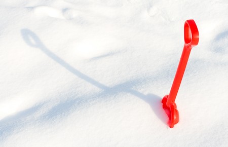 small red children shovel into a snow with shadowの写真素材