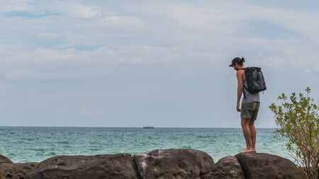 A backpacker is hiking along the coast, cloudy weather, ocean and rocksの写真素材