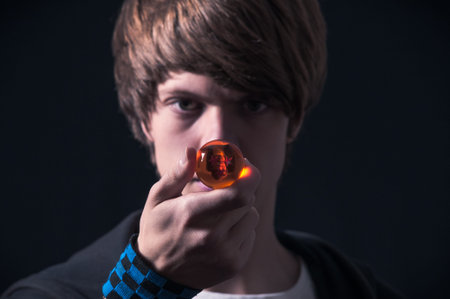 Blond boy with sweatshirt, showing a small ball, photographed in studio with black background
