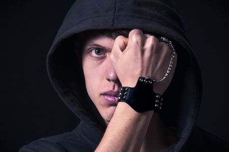 Blond boy with dark sweatshirt and hood photographed in studio with black backgroundの写真素材