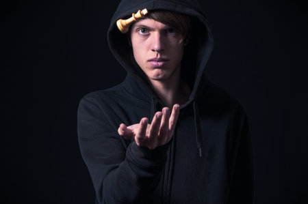 Blond boy with dark sweatshirt and hood photographed in studio, with black background, playing with...