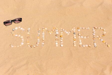 abstract word summer made of seashells on a sand with sunglassesの写真素材