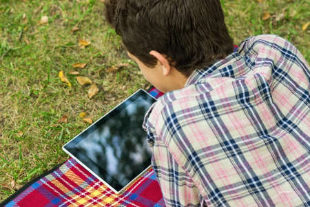 young men student sitting  in the park next to the tree with the tablet in his handsの写真素材