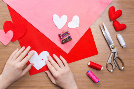 top view of hands pinning heart pattern felt fabric. sewing tools