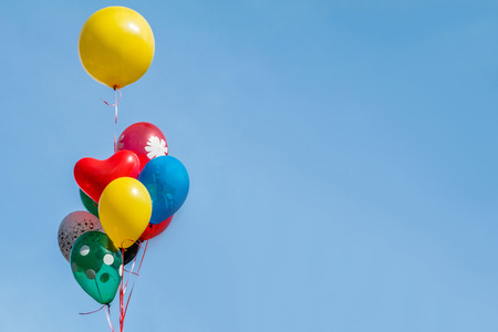 Colorful party balloon floating in mid air against a bright blue sky.の写真素材