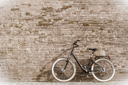 Black retro vintage bicycle with old brick wall and copy space. Retro bicycle with basket in front of the old brick wall. Old photo effect applied. Toned. の写真素材