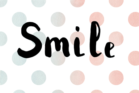 The word smile. Lettering. Brush calligraphy on colorful polka dot watercolor texture.の写真素材