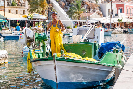 Symi, Greece - June 2021: Fisherman repairing fishing net on Symi Island near Rhodes, Greece.