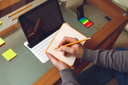 A man sitting at a desk, writing a pencil in a notebook. Mock up. Top view . Telework conceptの写真素材