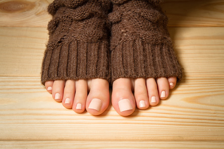 Beautiful beige pedicure. Legs in brown knitted socks on a wooden floorの写真素材
