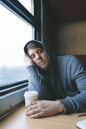 Man sleeping, sitting at a table in a train with a cup of coffeeの写真素材