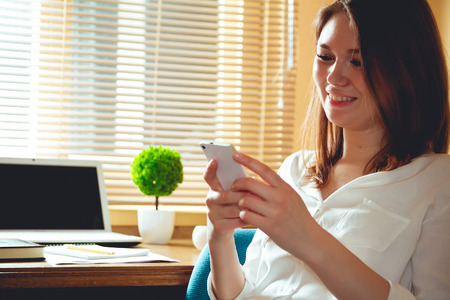 Young business woman, laughing, writing SMS while sitting at the table. Multitasking concept. Telework concept. Work at home. Break at workの写真素材