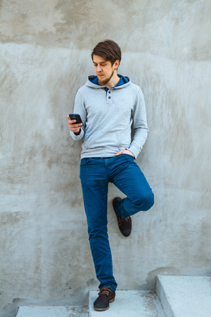 Young man writing sms standing by concrete wall. copy spaceの写真素材