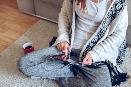 Woman in home cozy clothes sitting on the carpet near the sofa using a tablet with headphones,drinking coffee from a red cup. Online education concept. e-learning.の写真素材