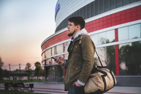 Portrait of a young man emerged from the airport with a phone in his hand and a bag.の写真素材