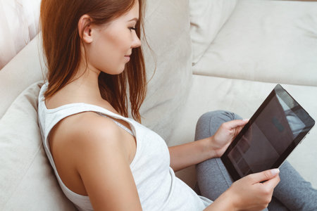 Young woman sitting on a couch and using tablet.