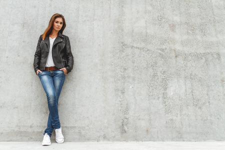 Portrait of a beautiful girl in jeans and a black leather jacket from the concrete wallの写真素材