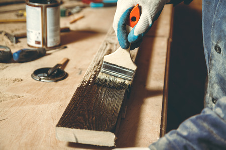 Man carpenter color brown paint wooden plank in his home workshopの写真素材