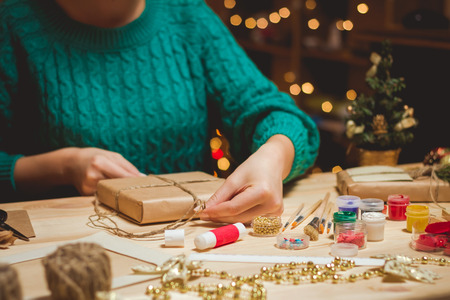 Girl sits at the table wraps Christmas presents. Handmadeの写真素材