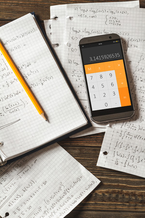 Solving mathematical problems in a notebook .  Phone with calculator app on wooden desk.の写真素材