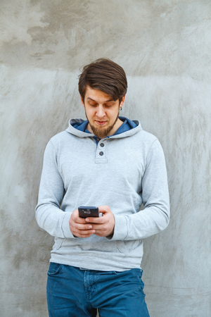Young man writing sms standing by concrete wall. copy spaceの写真素材