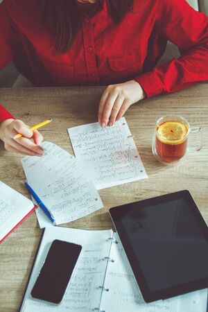 Pretty girl student doing homework sitting at table and drinking tea with lemonの写真素材