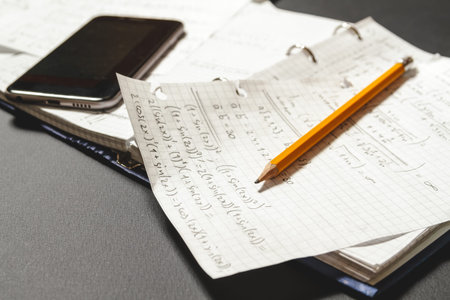 Solving mathematical problems in a notebook .  Phone with calculator app on desk.