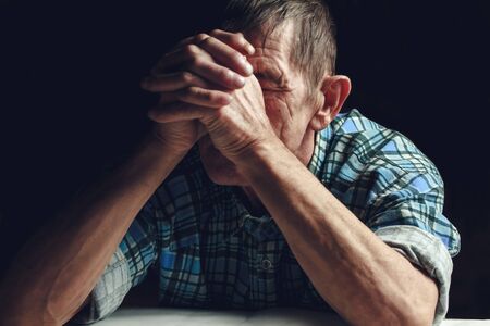 Depressed elderly man covers his face with his hands. Alzheimer's disease concept.の写真素材