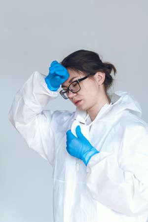 Tired female doctor in a protective suit, sitting on the floor, exhausted in the fight against a pandemic covid-19, leaning against the wall in a hospitalの写真素材