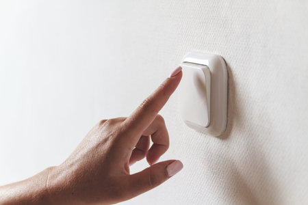 Female hand turns off the light indoors. Energy saving concept.