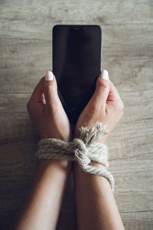 Tied female hands are holding a mobile phone. Smartphone addiction concept.の写真素材