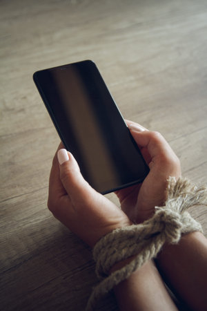 Tied female hands are holding a mobile phone. Smartphone addiction concept.