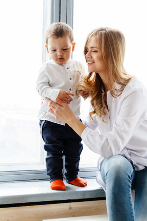 A young mother with a cute little son is having fun in a bright cozy living room near the window