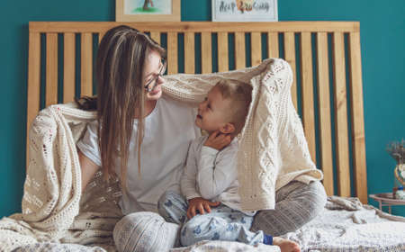 mom and child have fun in the bedroom on the bed, play under the blanketの写真素材