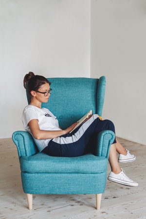 Young woman sitting in armchair and reading book, isolatedの写真素材