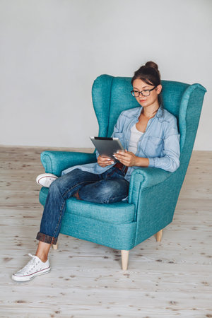 Young woman sitting in armchair and using tablet, isolated