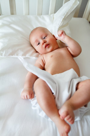 A cute kid lies in a wooden baby bed and plays with a pillowの写真素材