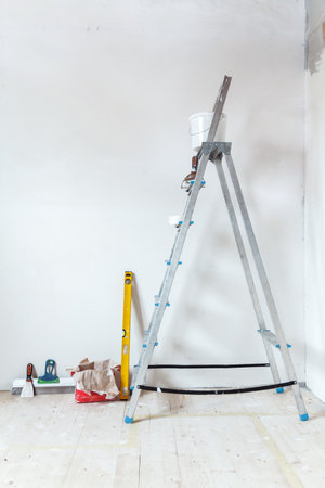 A stepladder with painting tools in a room in a house or apartment. Preparing for putty on the wall or painting. Home repair or renovation concept.の写真素材