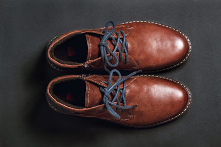 Brutal men's winter leather boots with blue laces on black background. Top view