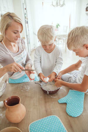 Yong mother with two sons cooking holiday pie in the kitchen. Casual lifestyle photo in real life...