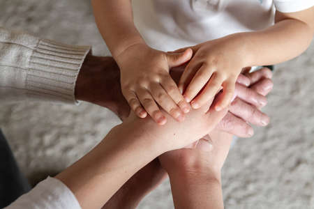 Grandfather, his daughter and little grandson together make a stack of palms and hands. Happy family togetherness. Happy family and support for elderly parents concept.の写真素材