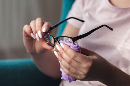 Young woman cleaning a glasses with a napkin while sitting in a chairの写真素材