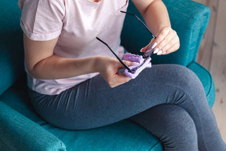 Young woman cleaning a glasses with a napkin while sitting in a chairの写真素材